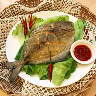 Ultra Crispy Fried Pomfret on lettuce on white plate with chilli sauce at the side