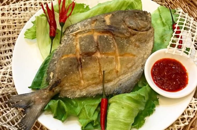 Ultra Crispy Fried Pomfret on lettuce on white plate with chilli sauce at the side