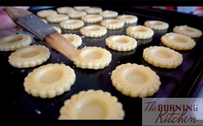 Placing pineapple tart cookie dough pieces on baking tray, brushing them with butter